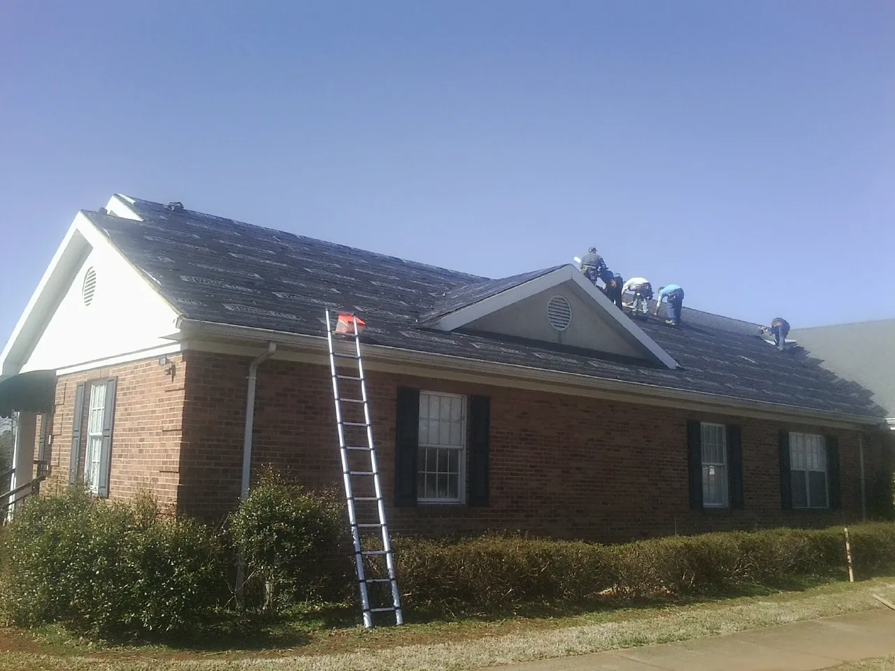 Crew tearing shingles off a brick ranch roof with a ladder set — Emergency Roof Repair work by our crew in Burbank