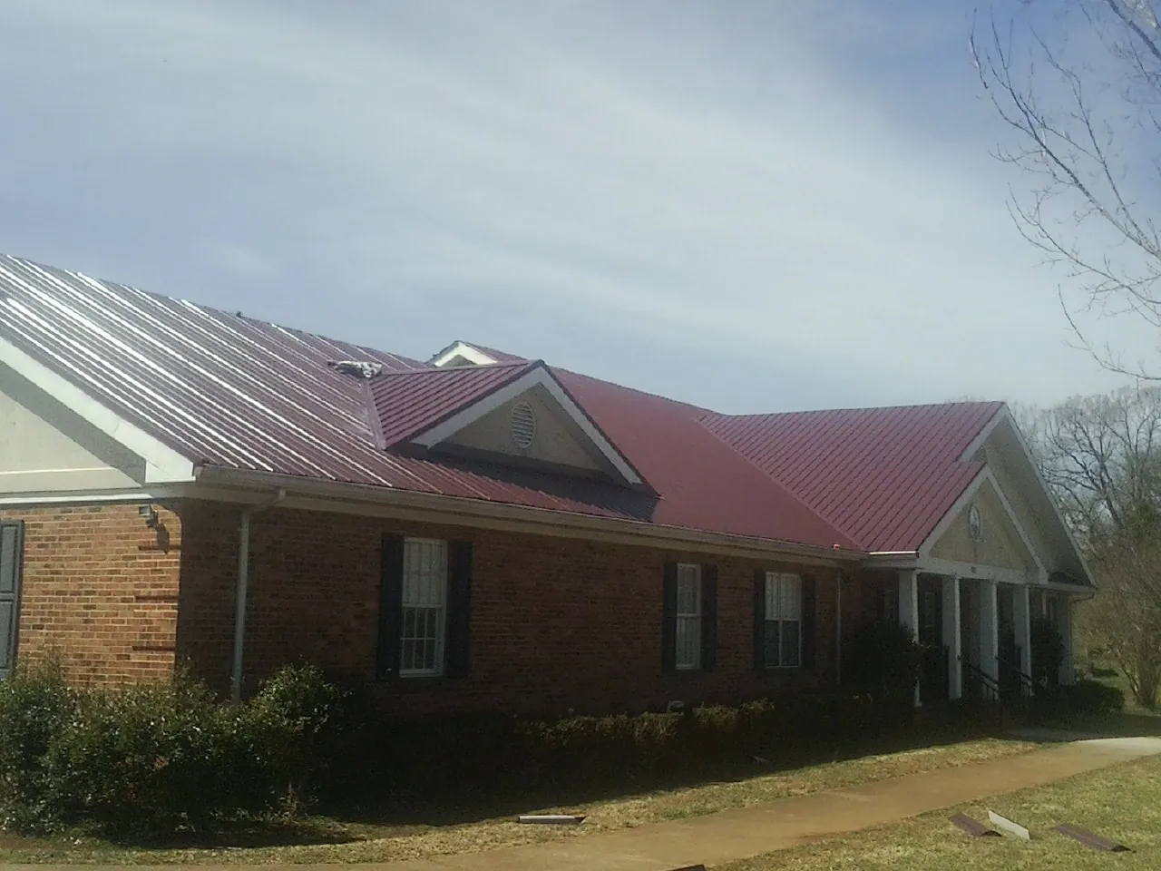 Red metal roof with gabled entries on a long brick building, from a Hail Damage Roof Repair job in Burbank